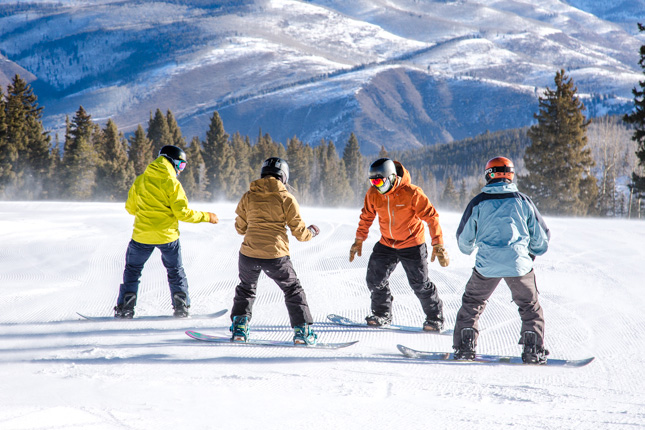 a snowboard instructor teaches three people how to snwoboard